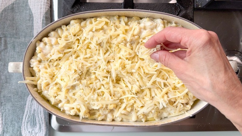Sprinkling shredded gruyere cheese on top of 3-ingredient mac and cheese in casserole dish