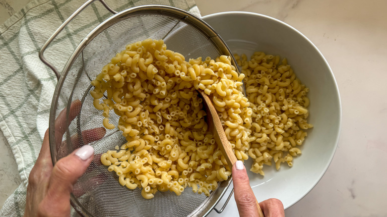 hand adding macaroni to bowl