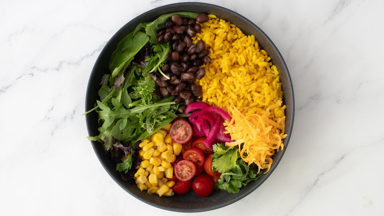 Lettuce, rice, beans, and other taco salad ingredients in bowl