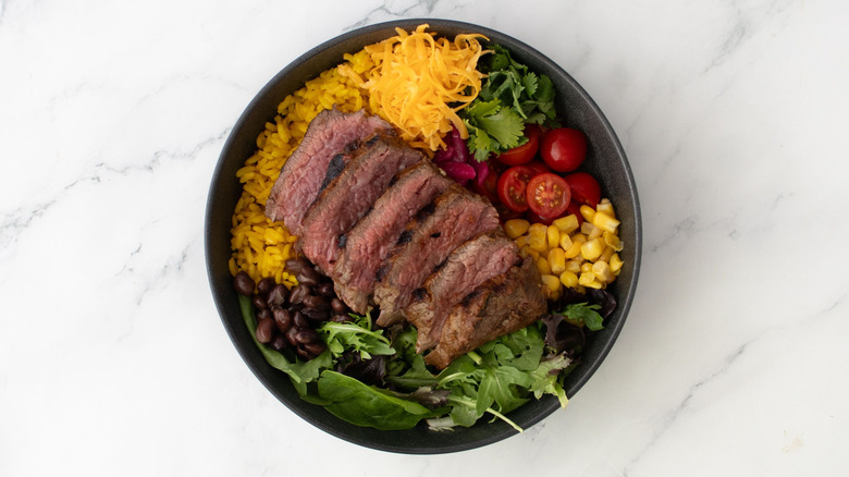 Taco salad in bowl topped off with sliced steak