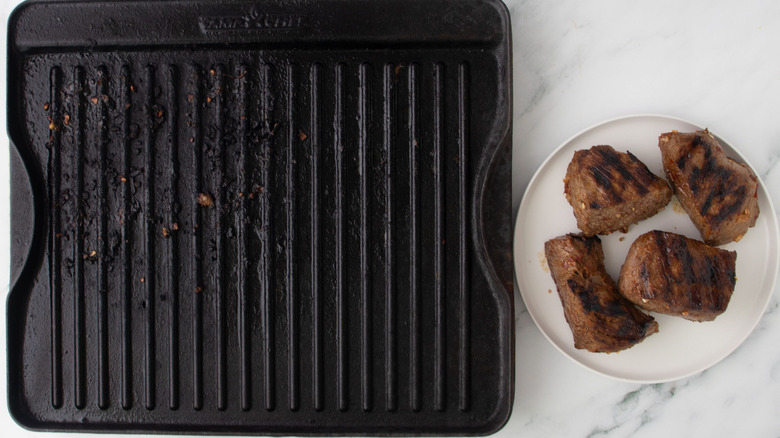 Steaks sitting on plate next to grill pan