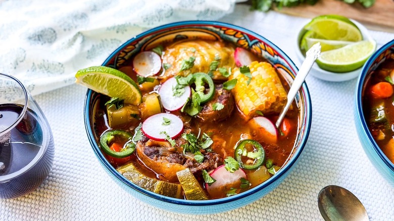 Caldo de Res in serving bowl with lime wedges and red wine