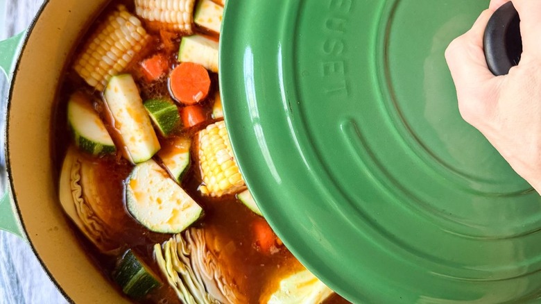 Placing green lid over Caldo de Res in Dutch oven