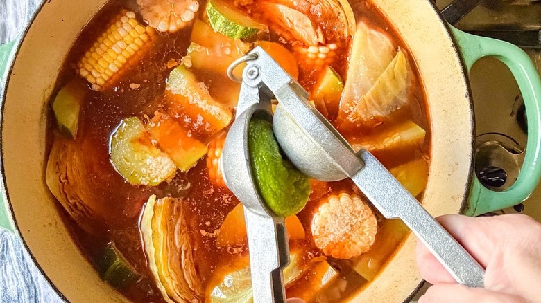 Squeezing fresh lime juice into Caldo de Res in Dutch oven on stovetop