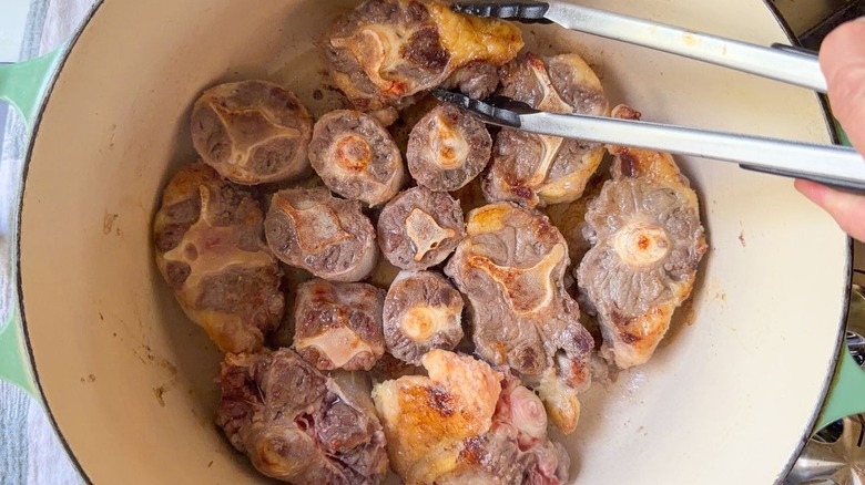 Crosscut beef shanks browning in Dutch oven on stovetop with tongs