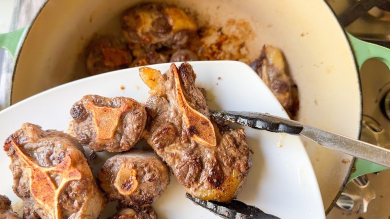 Placing browned crosscut beef shanks on plate with tongs
