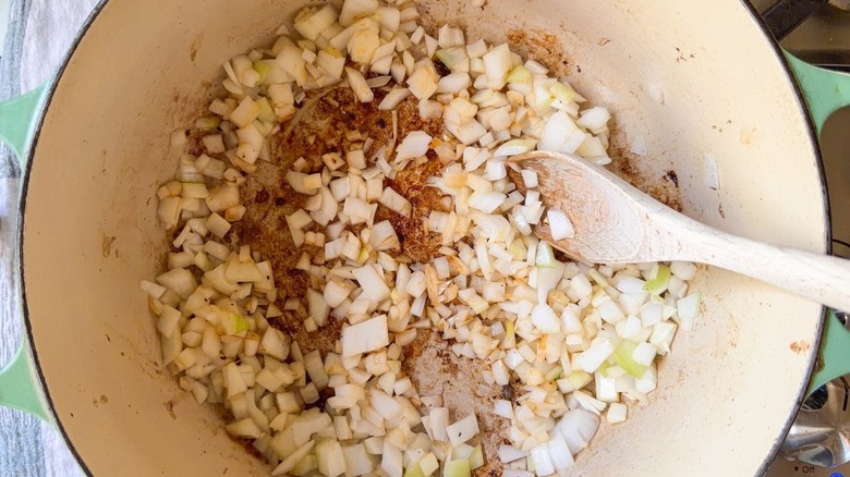 Stirring chopped onion in large pot on stovetop with wooden spoon
