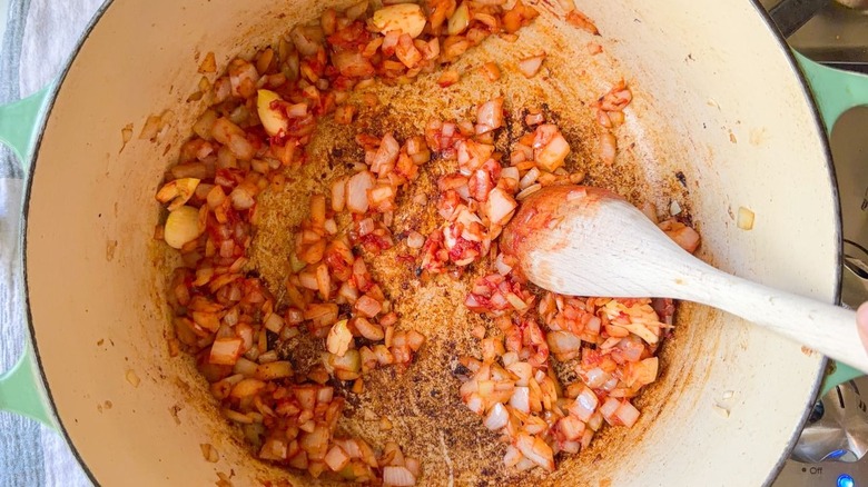 Stirring tomato paste into chopped onion in large pot with wooden spoon on stovetop