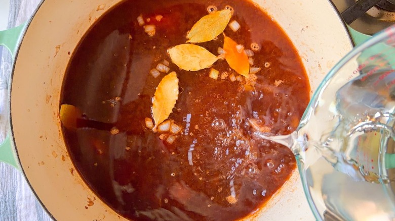 Adding water to Caldo de Res liquid and bay leaves in large pot on stovetop