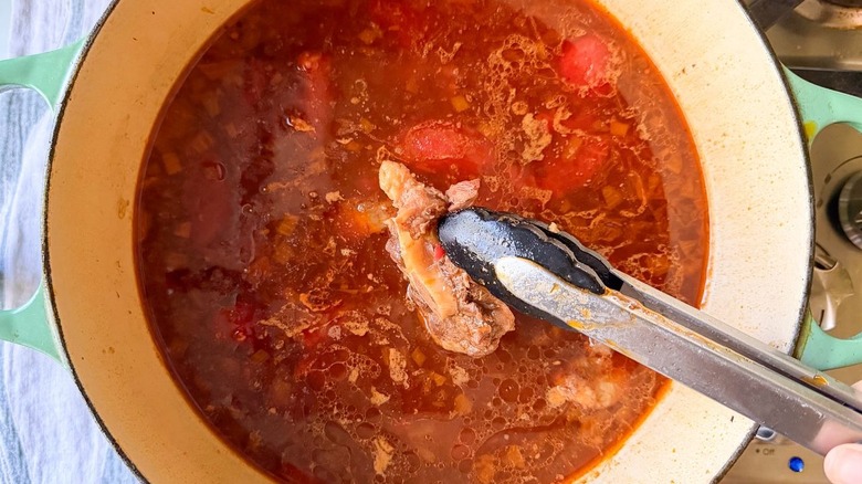 Pulling beef shank out of soup with tongs in Dutch oven on stovetop