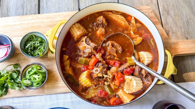 Pot of Caldo de Res on table with ladle and soup garnishes