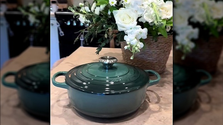 Le Creuset Dutch oven in artichaut on table with a basket of white flowers.