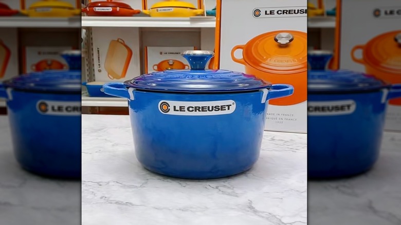 Azure Le Creuset on marbled counter in store with boxed items in the background.
