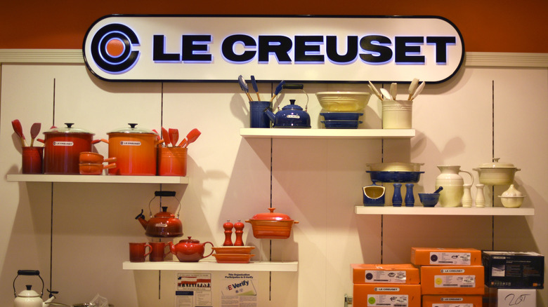 Various Le Creuset pots and pans in different colors displayed on shelves at the store.