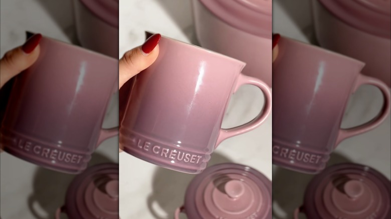 Hand holding a mauve ink Le Creuset mug.