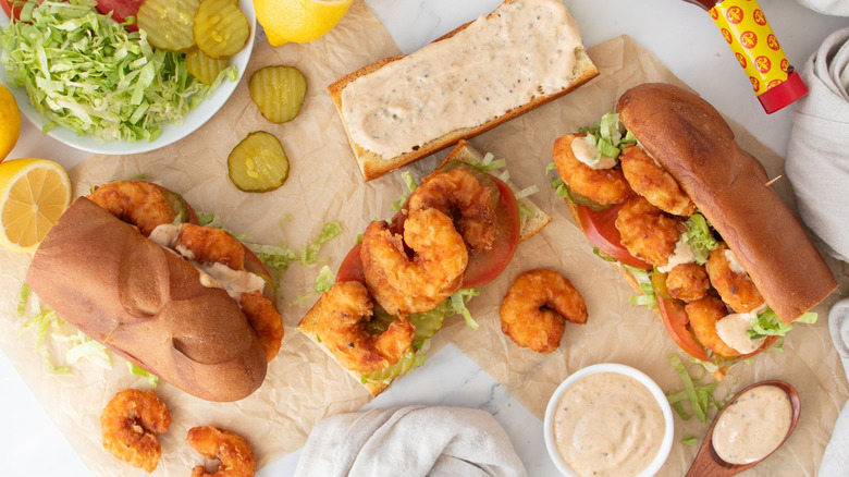 Fried shrimp po' boys surrounded by pickles, lemons, lettuce, and remoulade