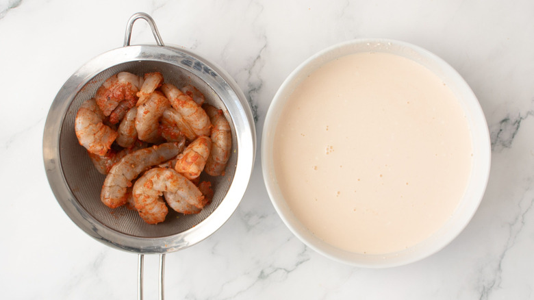 Shrimp in sieve next to buttermilk mixture in bowl