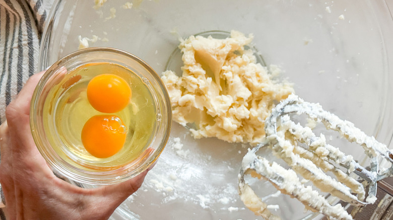 hand adding eggs to bowl with butter and sugar mixture