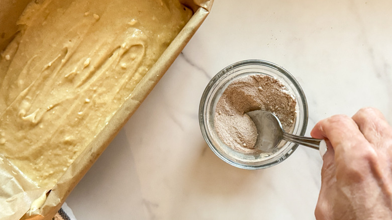 hand mixing cinnamon topping next to unbaked bread in loaf pan