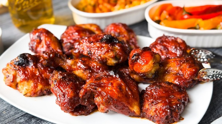 Honey bourbon BBQ chicken on serving platter with tongs and sides