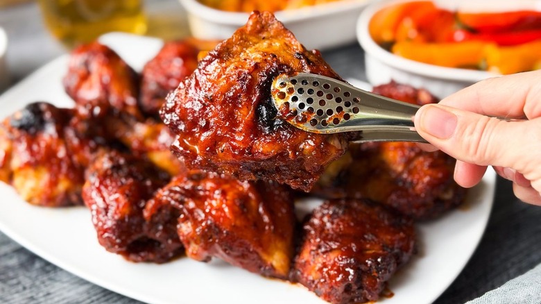 Honey bourbon BBQ chicken in tongs and on serving platter