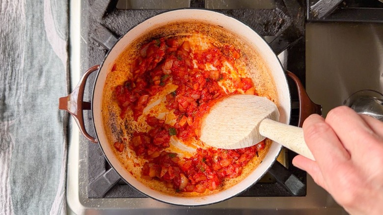 Stirring tomato paste into chopped onion and jalapeño with wooden spoon in pot on stovetop