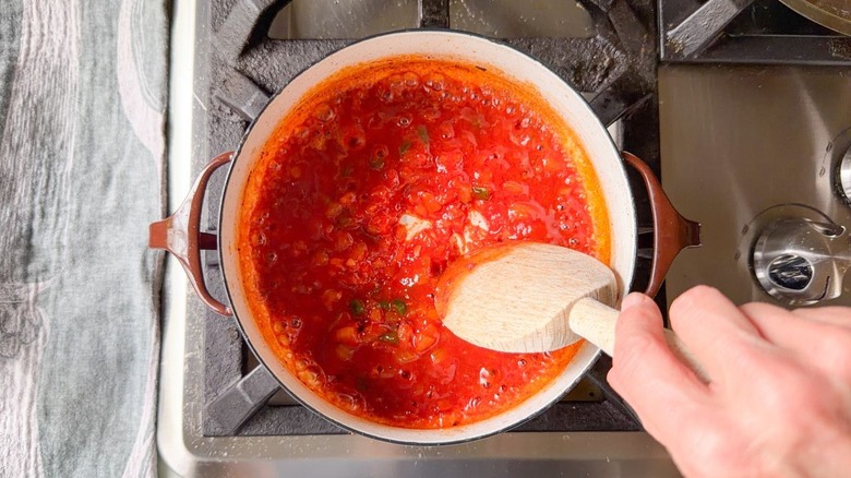 Stirring bourbon into BBQ sauce with wooden spoon in pot on stovetop