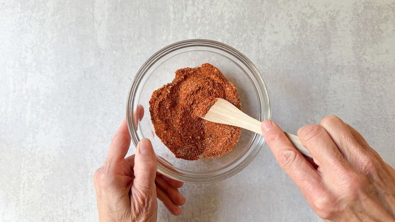 Mixing BBQ chicken spice rub in glass bowl with wooden spoon