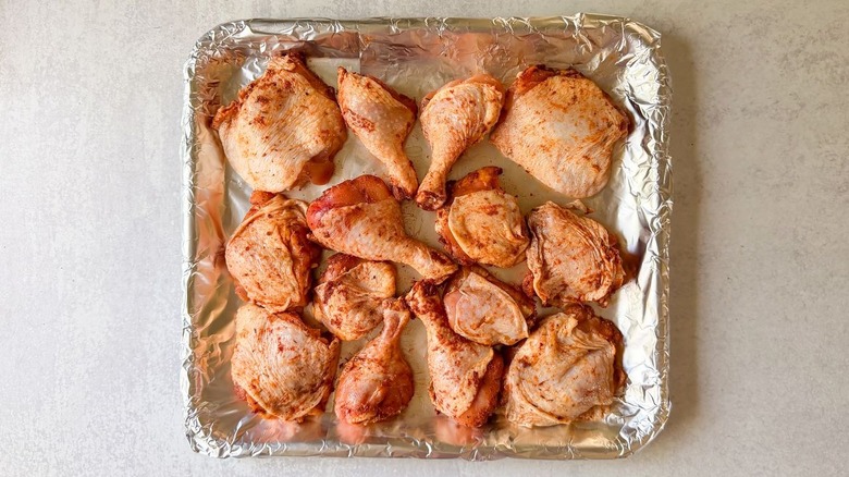 Skin-on chicken thighs and legs with spice rub on foil-lined baking sheet