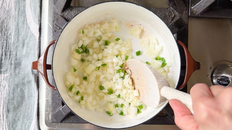 Stirring chopped onion, garlic, and jalapeño in pot on stovetop with wooden spoon