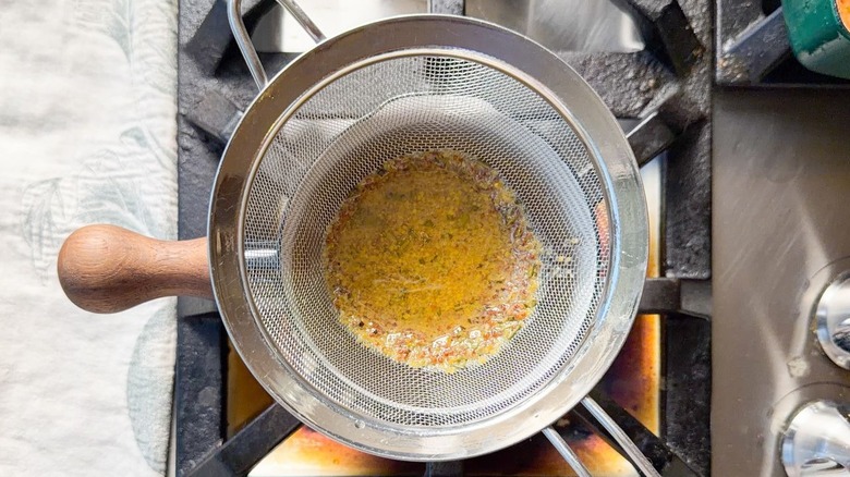 Straining ham pan drippings in fine mesh strainer over roasting pan