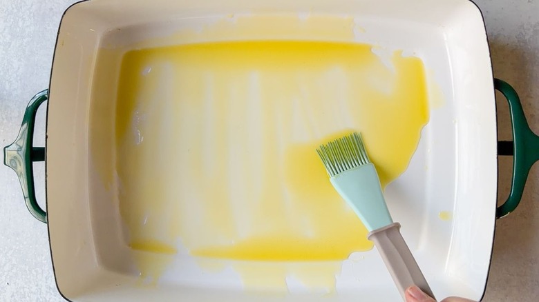 Brushing olive oil onto the bottom of a roasting pan with a pastry brush