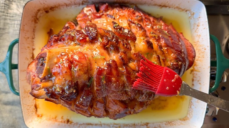 Brushing miso maple glaze on baked ham in roasting pan with pastry brush