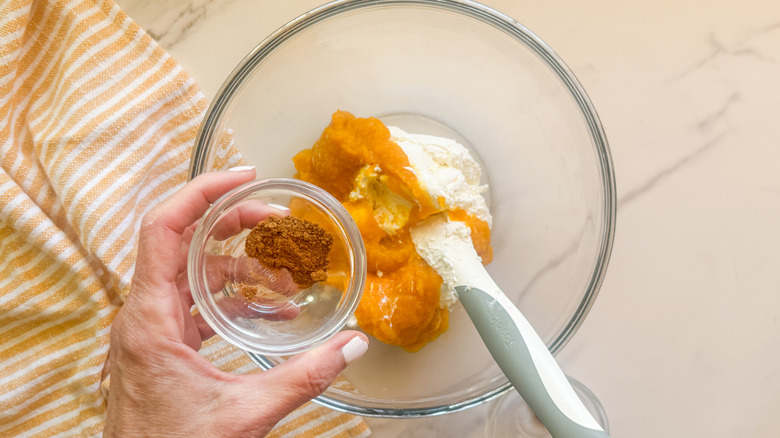 Pumpkin puree and cream cheese in bowl with cinnamon in smaller bowl