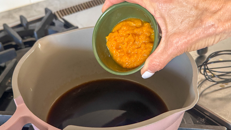 hand adding pumpkin to pot