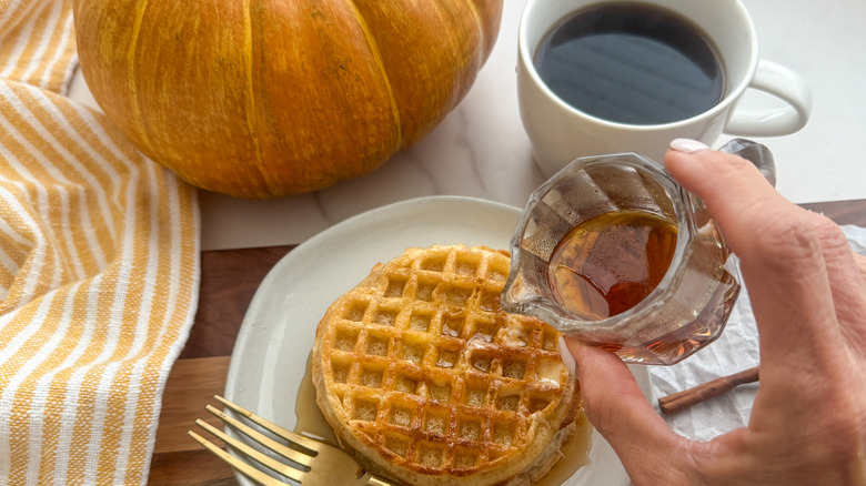 hand pouring syrup on waffles