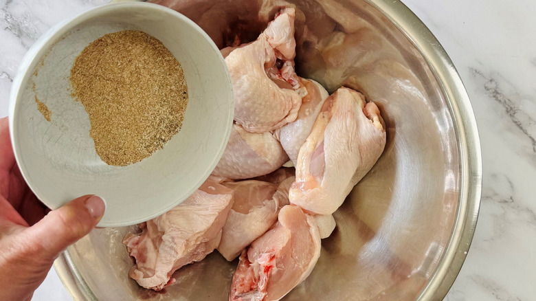Hand pouring bowl of seasoning over chicken pieces