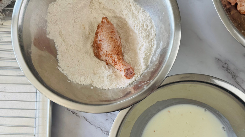 Chicken piece in flour bowl next to bowl of buttermilk