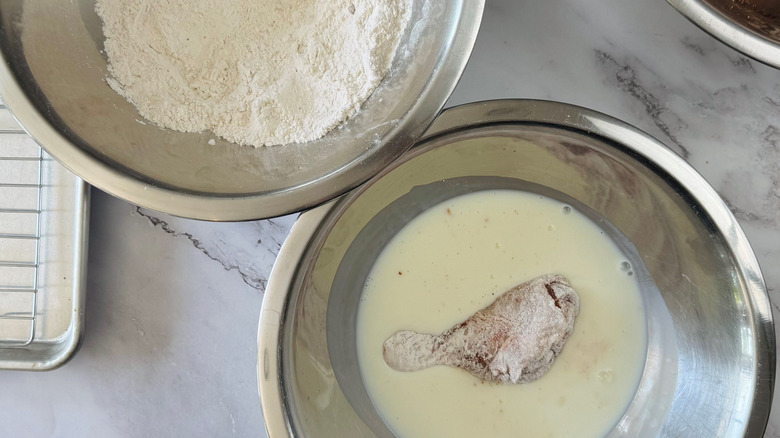 Flour coated chicken piece in bowl of buttermilk