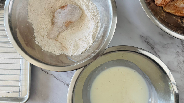 Coated chicken piece in flour next to bowl of buttermilk