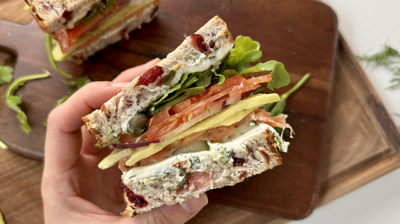 Hand holding smoked salmon sandwich half