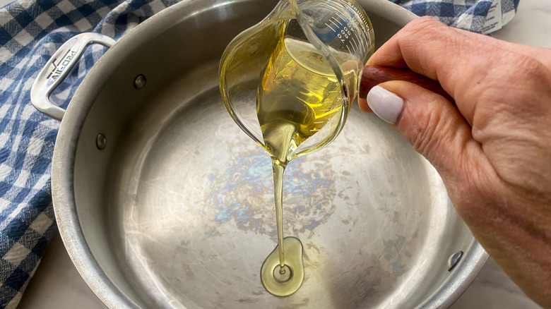 hand adding oil to skillet