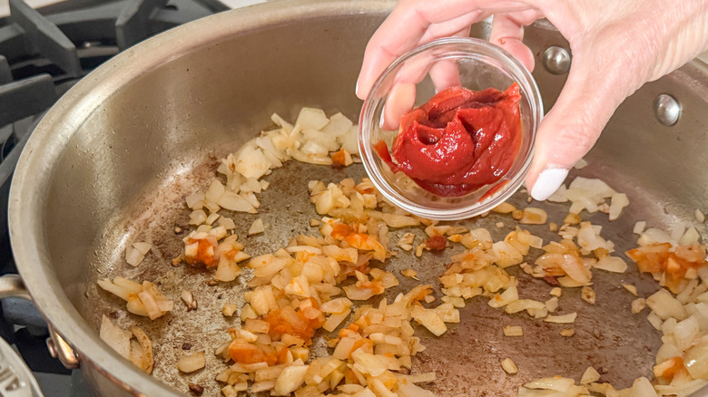 hand adding tomato paste