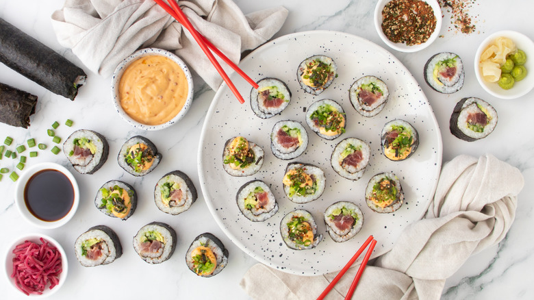 Spicy tuna roll sushi pieces on plate next to chopsticks and various bowls of sauce