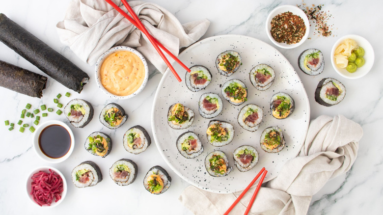 Spicy tuna roll pieces on plate next to chopsticks and bowls of sauce