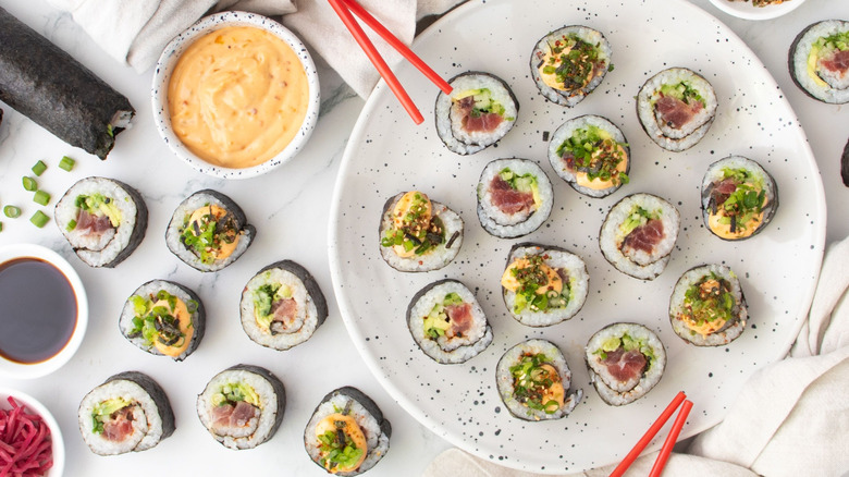 Spicy tuna roll pieces on plate next to chopsticks and spicy mayo