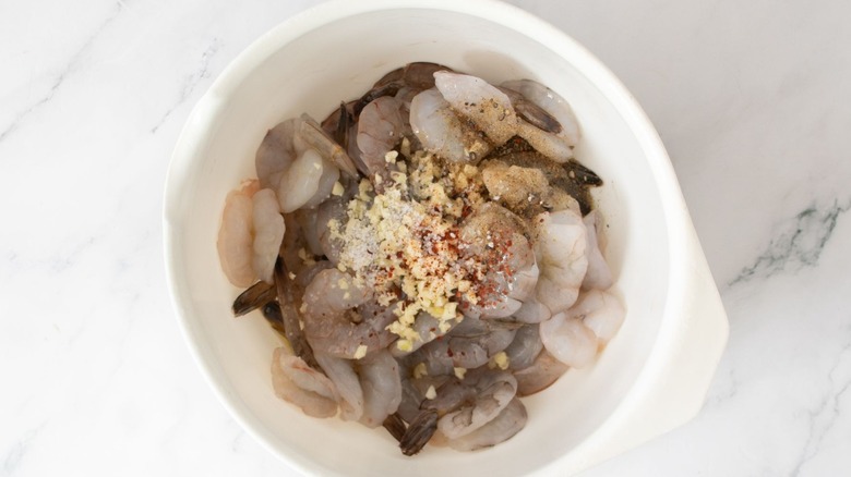 Raw shrimp with pile of seasonings on top in bowl