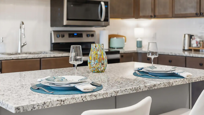 A white and black granite countertop with plates, wine glasses, and a vase