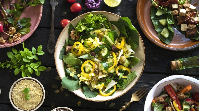 Plate of salad with banana pepper rings, cucumbers, and walnuts surrounded by more plates of various salads.