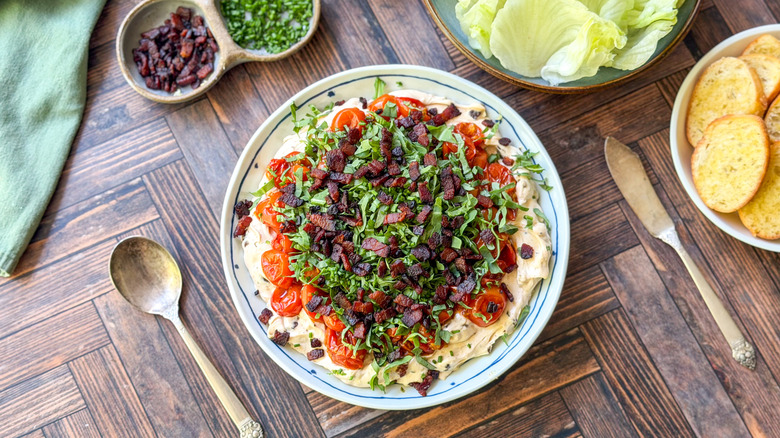 Over-the-top BLT dip in serving bowl with garnishes, lettuce cups, and toasts